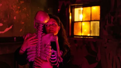 A woman in a pink lit room hugging a skeleton