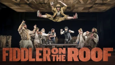 Theatrical promotional image for "Fiddler on the Roof," featuring the title in bold text against a vibrant stage background.