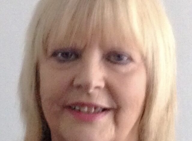 52 For 26 Poetry Project: Irene Stuart 1 Portrait headshot of a smiling blonde woman with straight hair, photographed against a plain light background. The image has soft lighting and a relaxed, friendly feel.